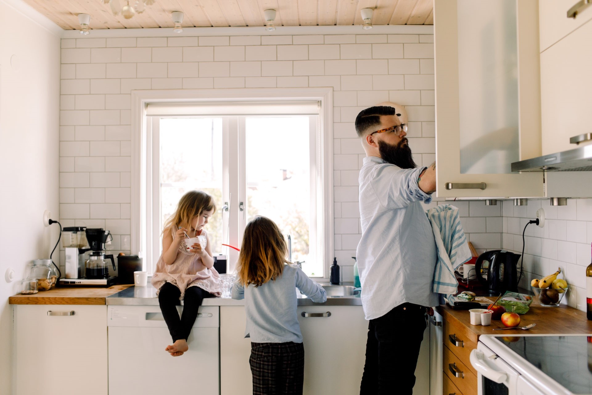 Girl looking at working sister while father doing chores in kitchen