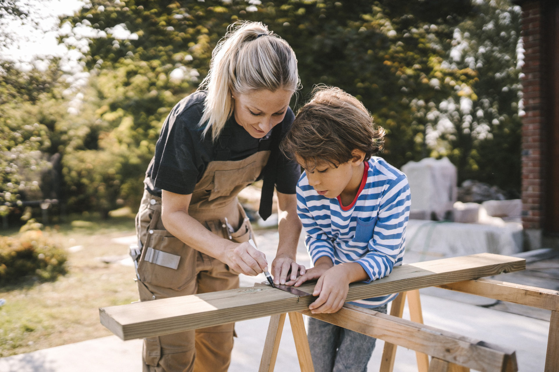 Mother measuring wooden plank by son at construction site