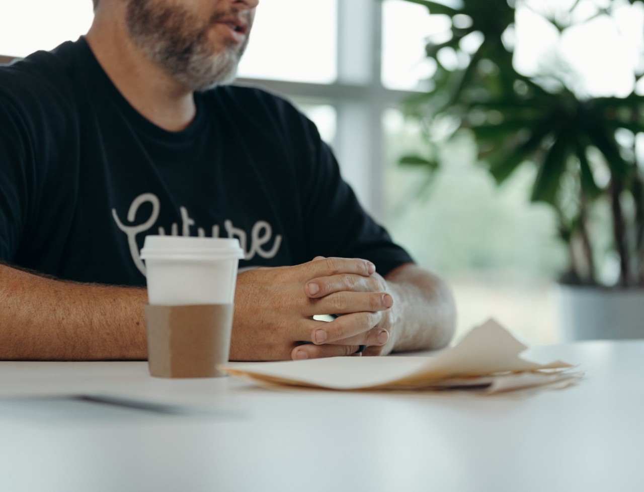 Man seated at a table with hands together and a coffee